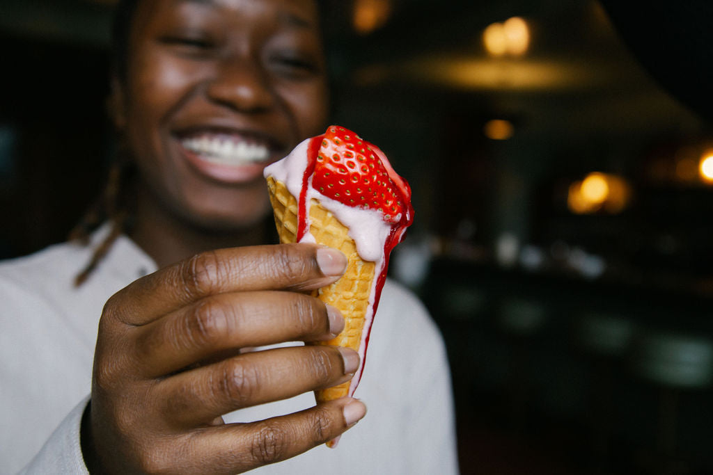 Smiling person holding up flavorful vegan dairy free strawberry ice cream in cone with strawberry garnish