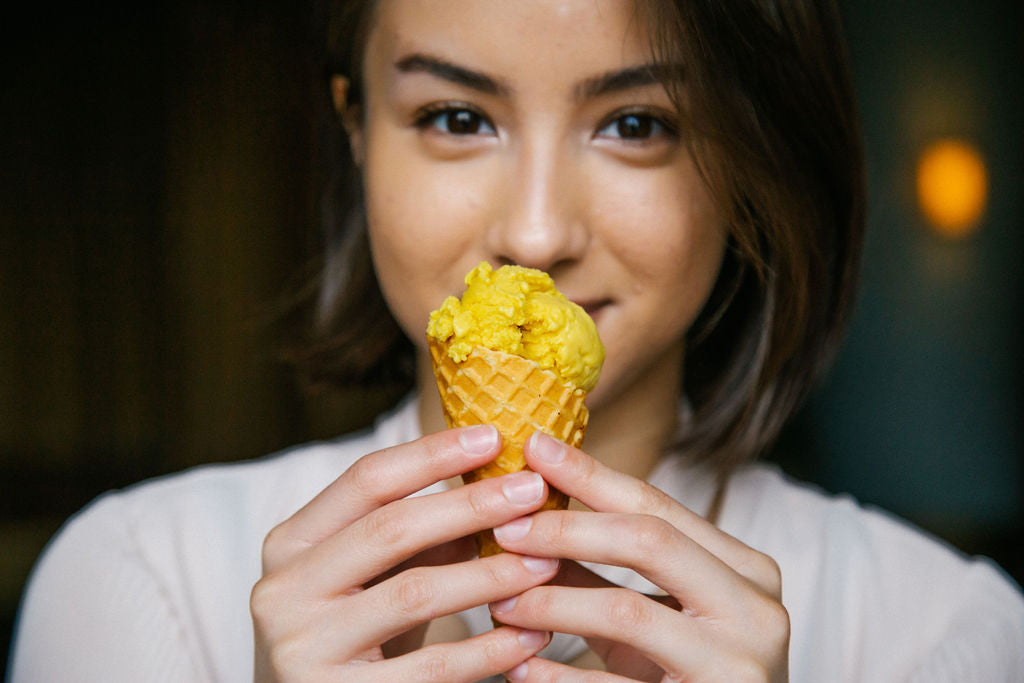 Person smiling behind a cone full of plant based mango ice cream 