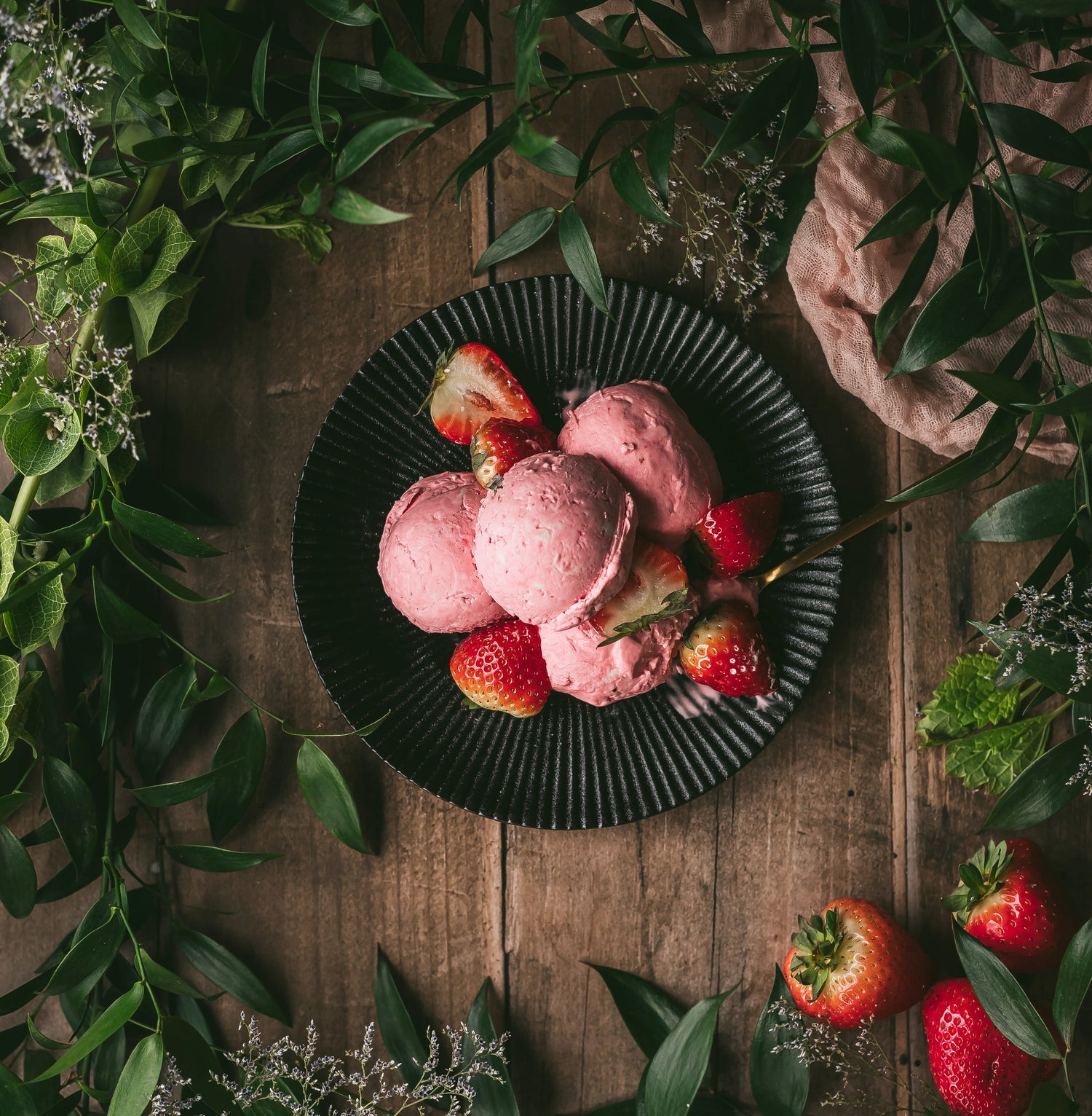 Plant based strawberry ice cream with strawberry garnish surrounded by greenery on picnic table
